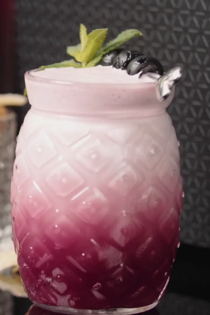 A blueberry and ginger cooler with a foam head in a textured tumbler
