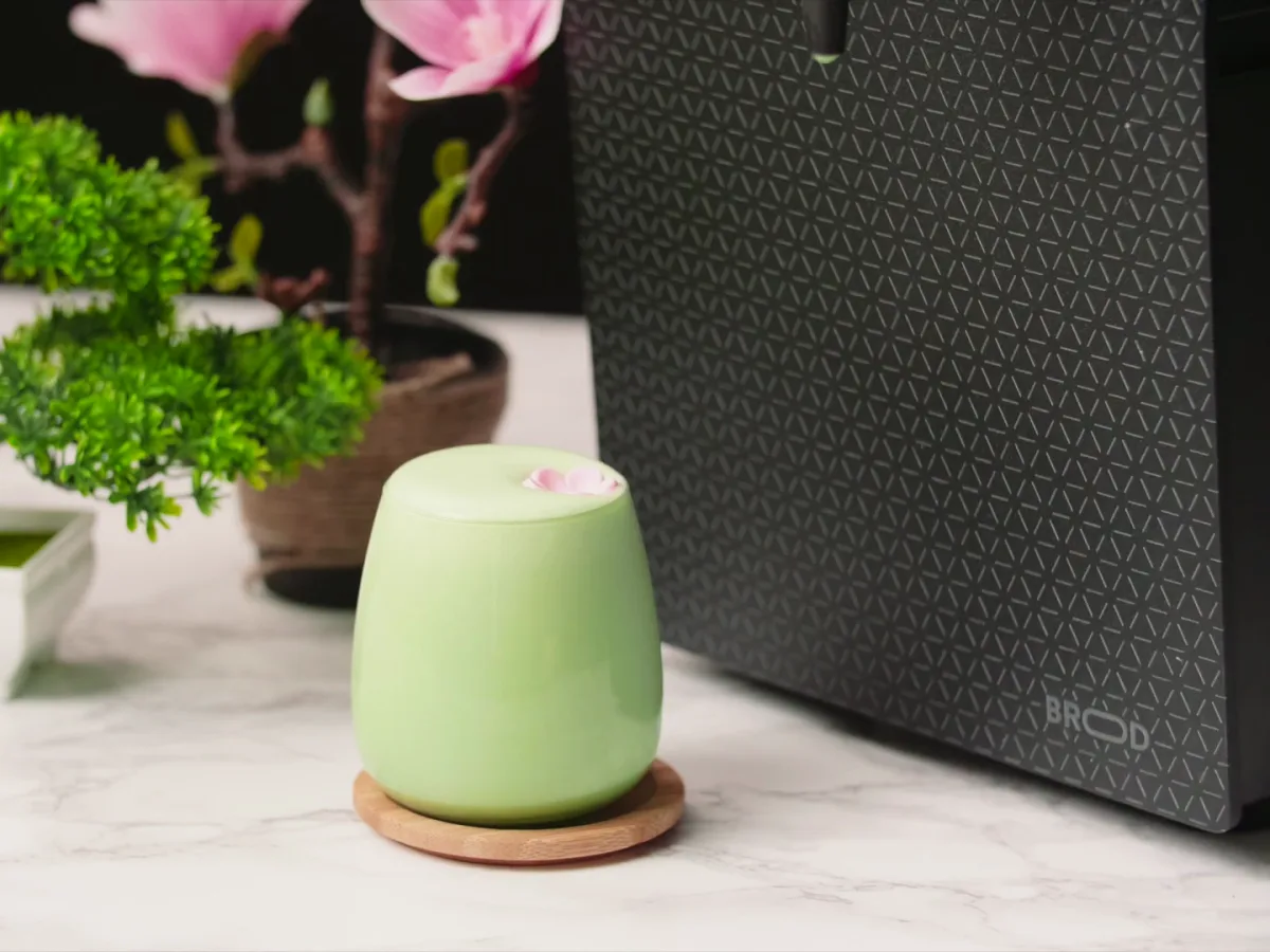 A matcha latte in a pale green cup on a wooden coaster, beside a DRNX machine